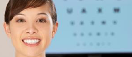 eye care practitioner smiling in front of an eye exam chart